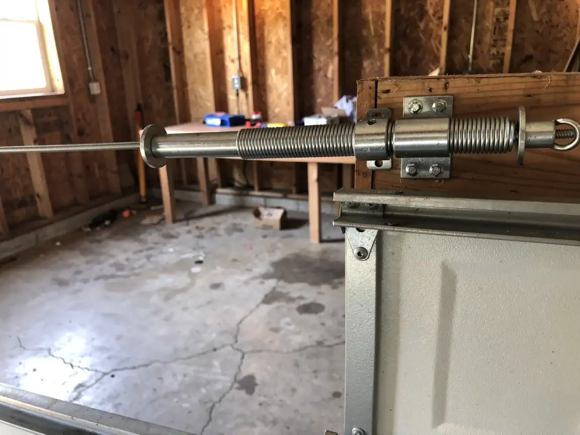 An extension spring is mounted above a white garage door inside a garage.